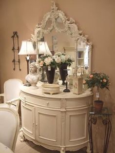 a white dresser topped with vases filled with flowers next to a wall mounted mirror