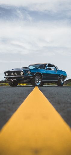 an old blue car is parked on the side of the road next to a yellow arrow