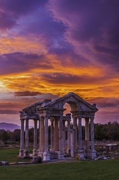 an old building sitting in the middle of a lush green field under a colorful sky