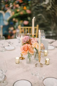 the table is set with white plates and silverware, candles and flowers in vases