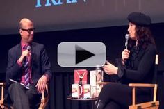 two people sitting in chairs talking to each other at an event with a screen behind them