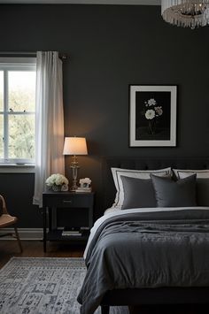 a bedroom with black walls and gray bedding, chandelier, chair, rug and window