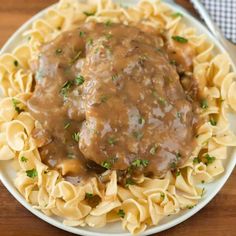 a white plate topped with meat and gravy covered in sauce on top of pasta