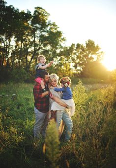 a family is posing for a photo in the grass with their child on their shoulders