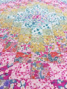 a multicolored patchwork quilt is laying on top of a tablecloth that has flowers all over it