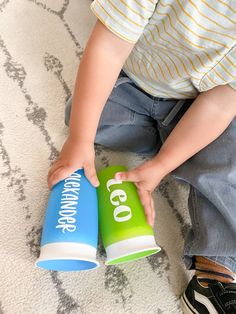 a small child is playing with two cups on the floor and one has his hand in it