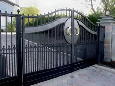 an iron gate with two circular knobs on the top and bottom, leading to a driveway