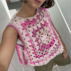 a woman wearing a pink and white crocheted vest with flowers on it's chest