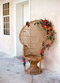 a wicker chair sitting next to a wall with flowers on the back and seat