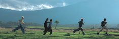 four people are running in the grass with mountains in the backgrouds behind them