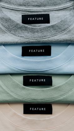 four t - shirts with black labels on them are stacked up in different colors and sizes