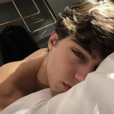 a young man laying in bed with his head on the pillow and looking at the camera