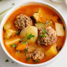 a bowl of soup with meatballs and vegetables on the side, ready to be eaten