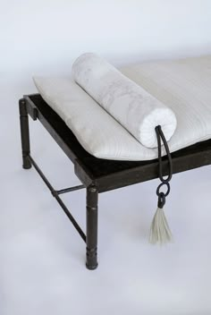 a black metal bench with a white pillow on it's back and a tassel hanging from the seat