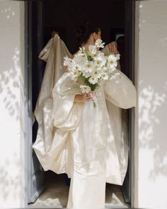 a woman in a white dress holding a bouquet of flowers while standing at the door