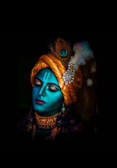 the face of a woman with blue paint and feathers on her head, wearing an orange turban