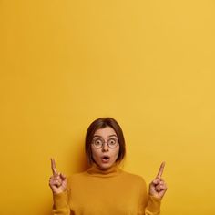 a woman with glasses holding two fingers up in front of her face and pointing to the side