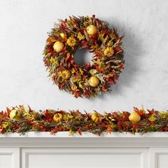 a wreath is hanging on the wall above a mantle with autumn leaves and pumpkins