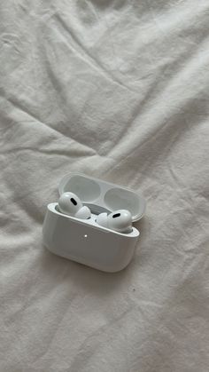 an earbud case sitting on top of a white sheet with two headsets in it