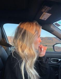 a blonde woman sitting in the passenger seat of a car talking on her cell phone