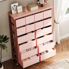 a pink dresser with drawers and pictures on the top shelf next to a potted plant