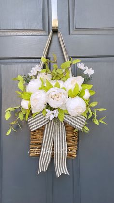 a basket filled with white flowers hanging from a door handle on a gray front door