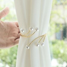 a person is holding onto a curtain with pearls on it and gold colored metal hardware