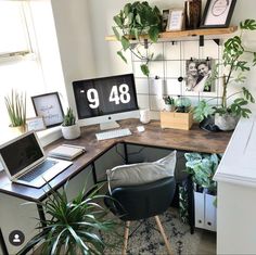 a desk with a laptop, computer monitor and plants on it in front of a window