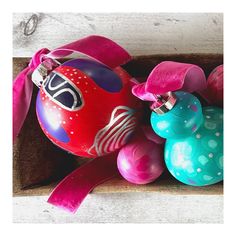 an assortment of ornaments in a box on a wooden surface with pink and blue ribbons