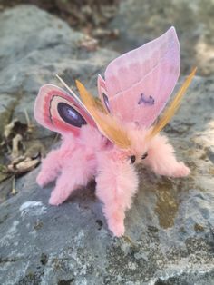 a pink stuffed animal with a butterfly on it's head sitting on some rocks