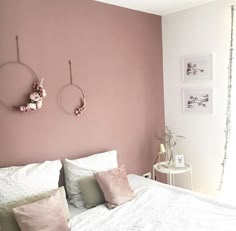 a bedroom with pink walls and white bedding, two hanging decorations on the wall