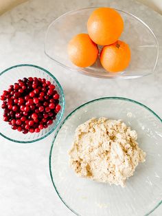 oranges, cranberries and dough in bowls on a marble counter top with other ingredients