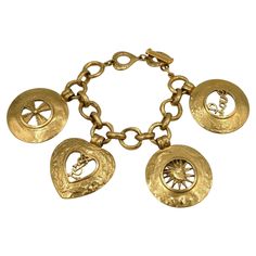 YVES SAINT LAURENT vintage gold toned link bracelet featuring fours charms : cross, YSL logo, sun face and Love. T- bar closure and heart toggles. Marked with the YVES SAINT LAURENT cursive signature on the heart toggles. Embossed Made in France. Indicative measurements : length from approx. 19 cm (7.48 inches) to approx. 21 cm (8.27 inches) / medallions diameter approx. 4 cm (1.57 inches) / heart approx. 4 cm x 4 cm (1.57 inches x 1.57 inches). NOTES - This is a preloved vintage item, therefore Ysl Charm Bracelet, Cursive Signature, Ysl Vintage, Saint Laurent Vintage, Sun Face, Ysl Logo, Vintage Charms, Link Bracelets, Arm Band