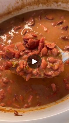 a spoon full of soup with beans and meats in it, on top of a white plate