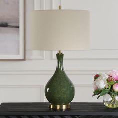 a green vase with flowers sitting on top of a table next to a white lamp