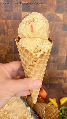 a hand holding an ice cream cone with peaches in the background