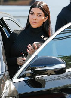 a woman is looking at her cell phone while getting out of a car in the parking lot