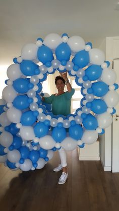 a woman standing in front of a bunch of blue and white balloons on top of a wooden floor