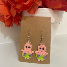 a pair of pink and green earrings sitting on top of a card next to flowers