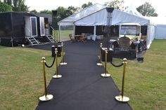 an outdoor event with black carpet and gold poles on each side, white tents in the background