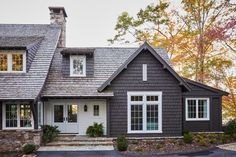 a gray house with white doors and windows in the front yard is surrounded by autumn foliage