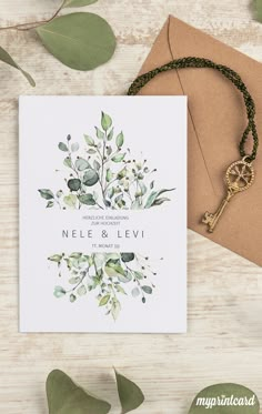 a wedding card with greenery on it and a key hanging from the front, next to an envelope