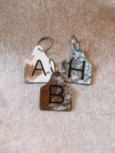 three keychains with letters on them are sitting on a carpeted floor and one has a cowhide tag