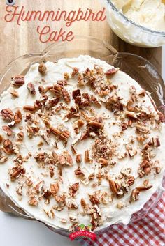 hummingbird cake with white frosting and pecans in the middle on a red checkered tablecloth