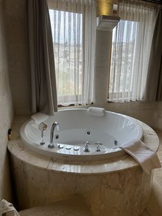 a large white bath tub sitting next to a window with sheer curtains on the windowsill