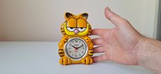 a hand holding a small yellow tiger clock