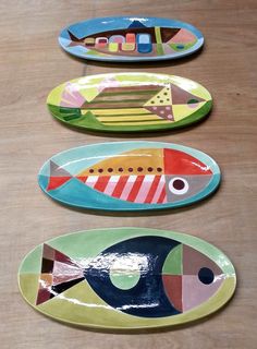 three plates with fish painted on them sitting on a wooden table next to each other