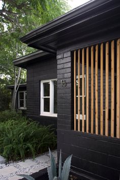 a small black house with wooden slats on the front door and side windows, along with succulents