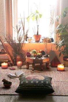 a living room filled with lots of plants and candles on top of a rug next to a window