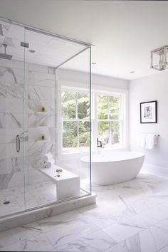 a large white bathroom with marble flooring and glass shower doors, windows, and a freestanding tub